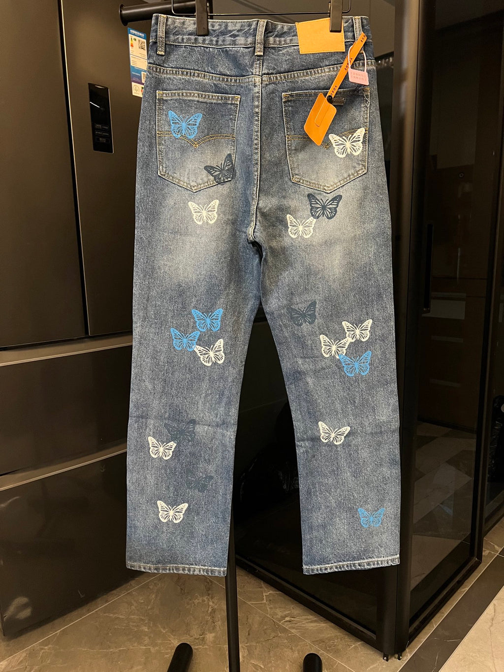 Blue denim pants with butterfly patches, back pocket detail, and tag on hanger