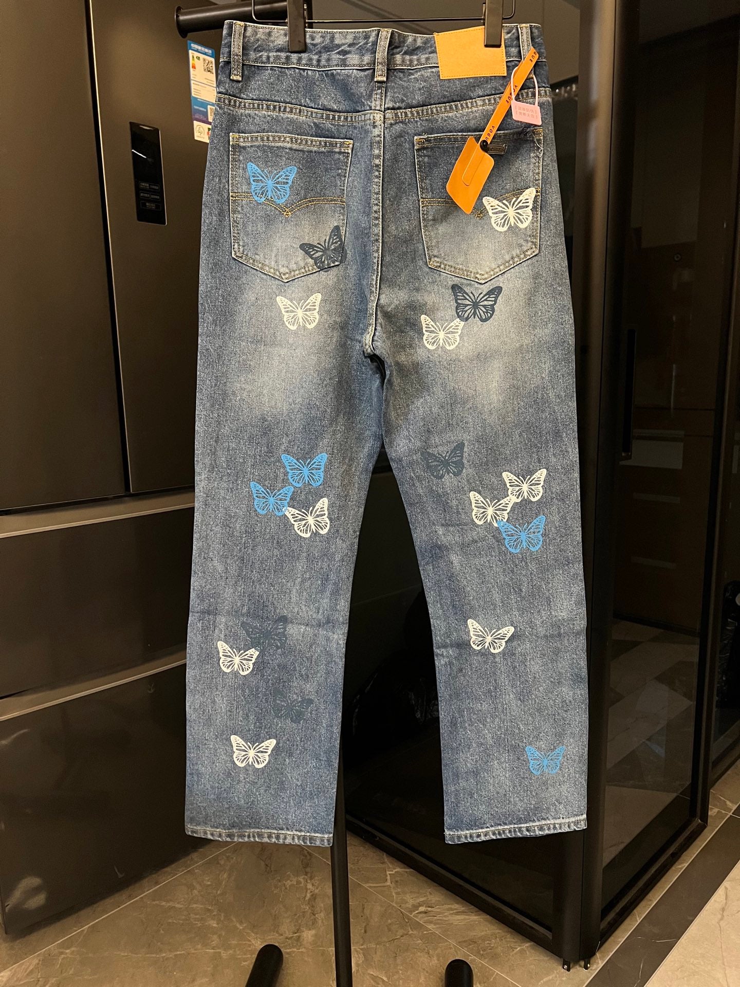 Blue denim pants with butterfly patches, back pocket detail, and tag on hanger