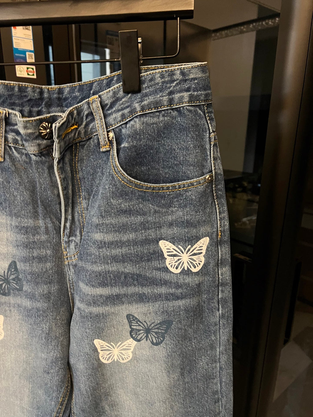 Blue denim pants with butterfly patches on front pocket and thigh, zipper fly