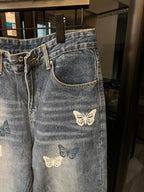 Blue denim pants with butterfly patches on front pocket and thigh, zipper fly