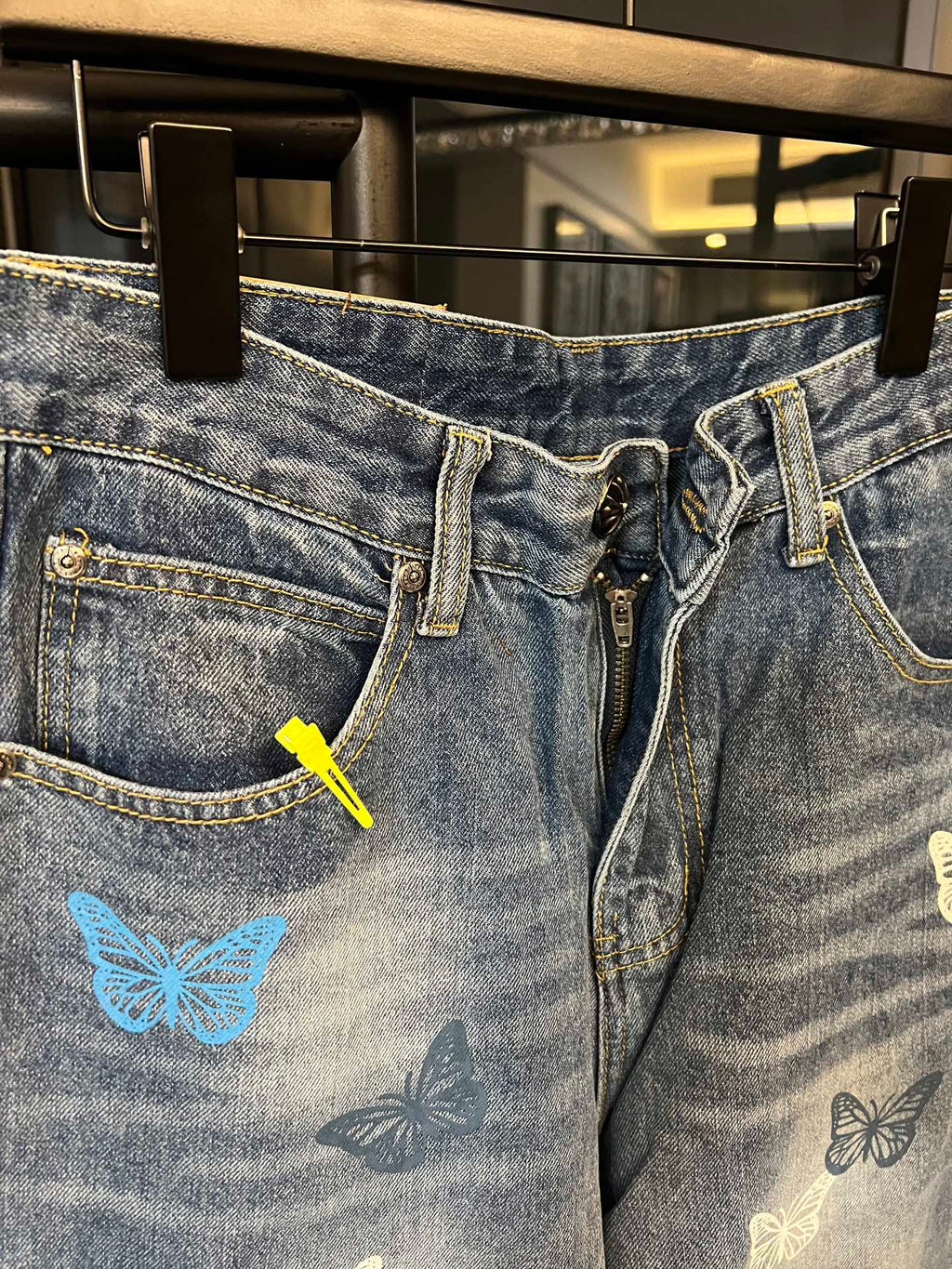 Front view of blue denim pants with butterfly graphic, zipper, and belt loops