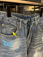 Front view of blue denim pants with butterfly graphic, zipper, and belt loops