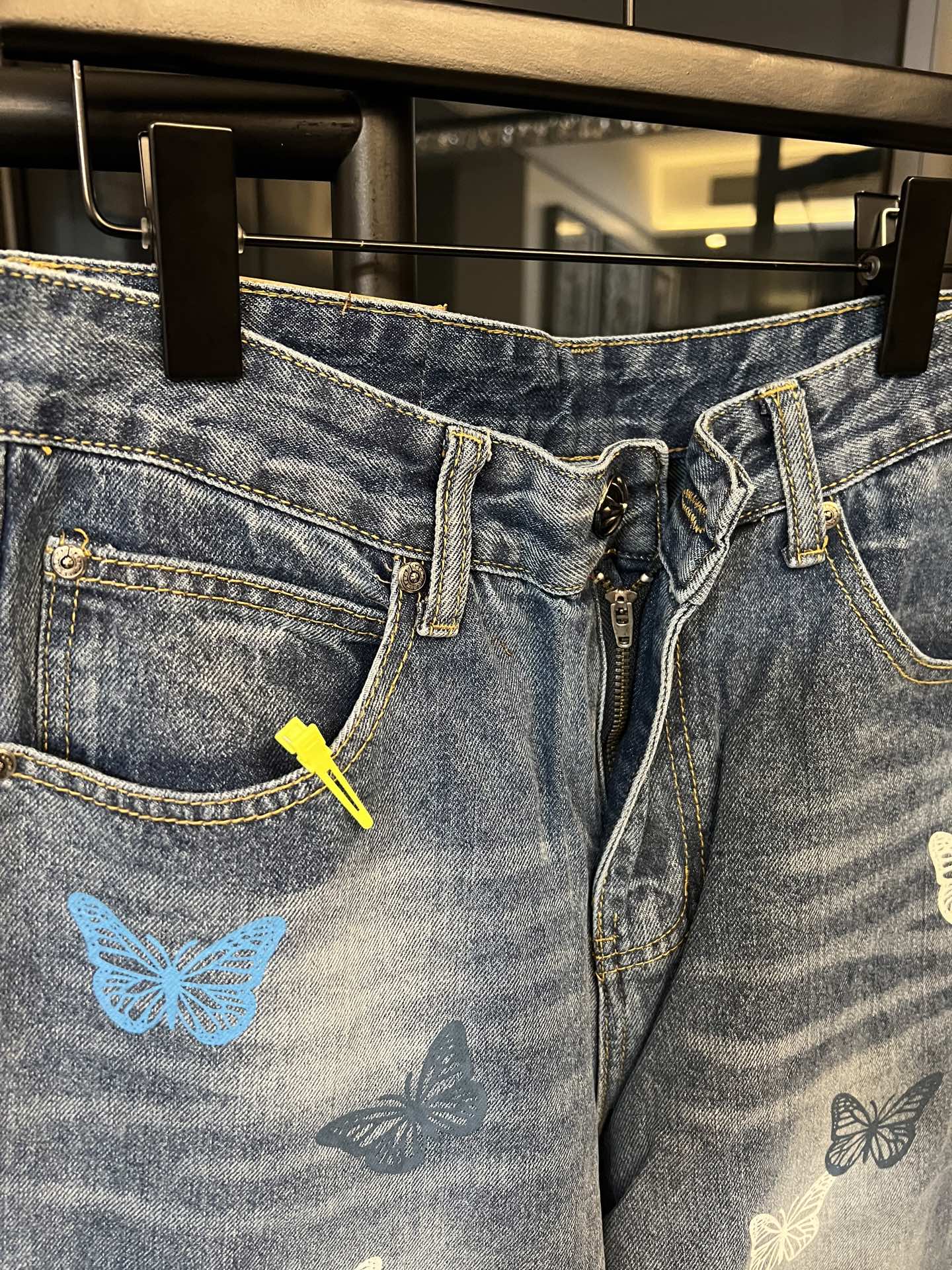 Front view of blue denim pants with butterfly graphic, zipper, and belt loops