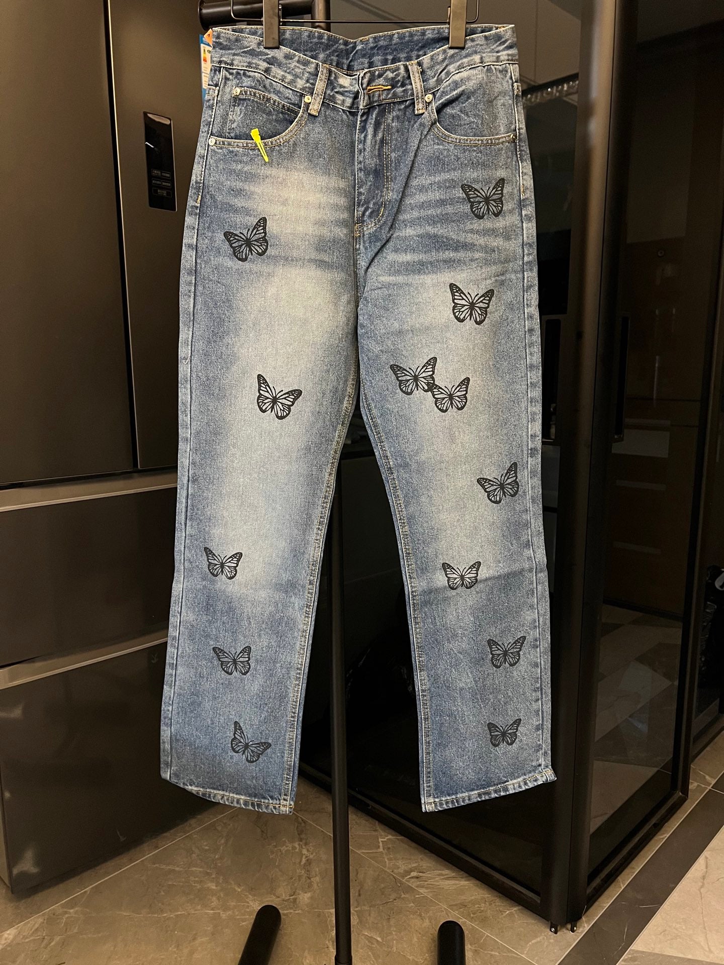 Light blue denim pants with black butterfly embroidery, front pockets, and belt loops