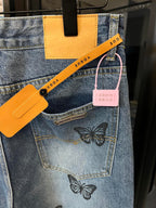Light blue denim jeans with black butterfly embroidery and a hanging price tag over waistband