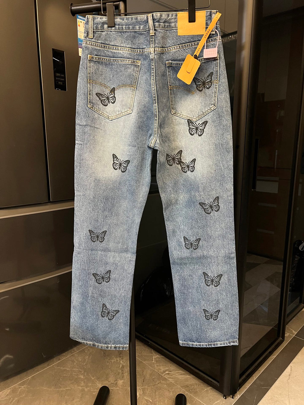 Light blue denim jeans with black butterfly embroidery and front pockets, hanging tags attached