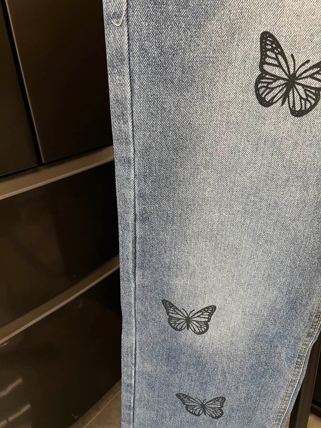 Light blue denim pant leg with black butterfly embroidery near midsection