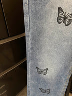 Light blue denim pant leg with black butterfly embroidery near midsection