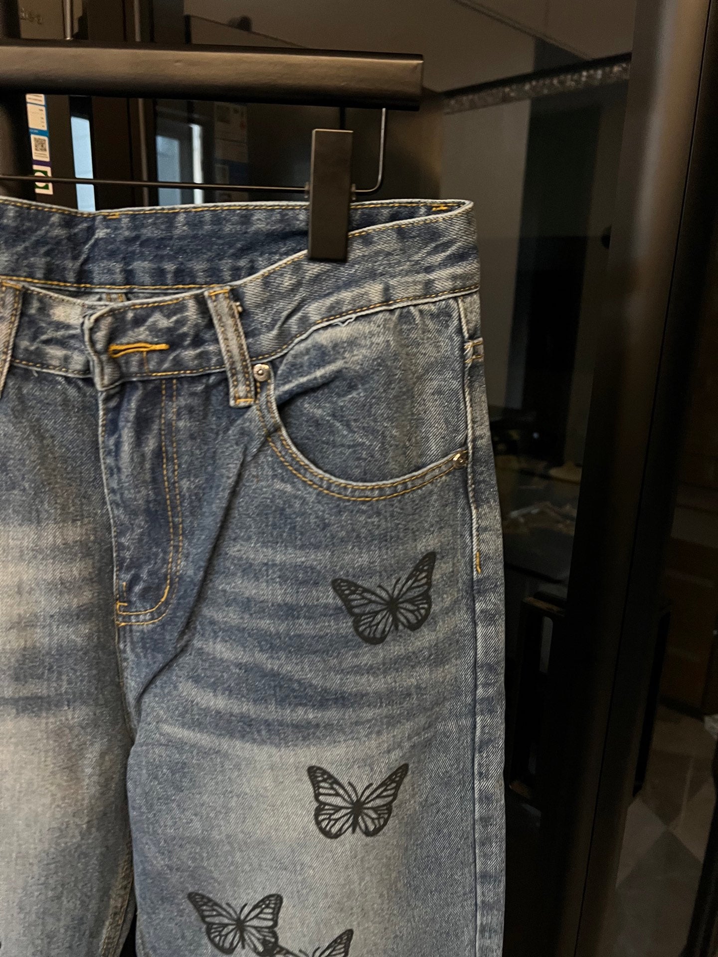 Light blue denim jeans with black butterfly embroidery on front leg, front pocket view
