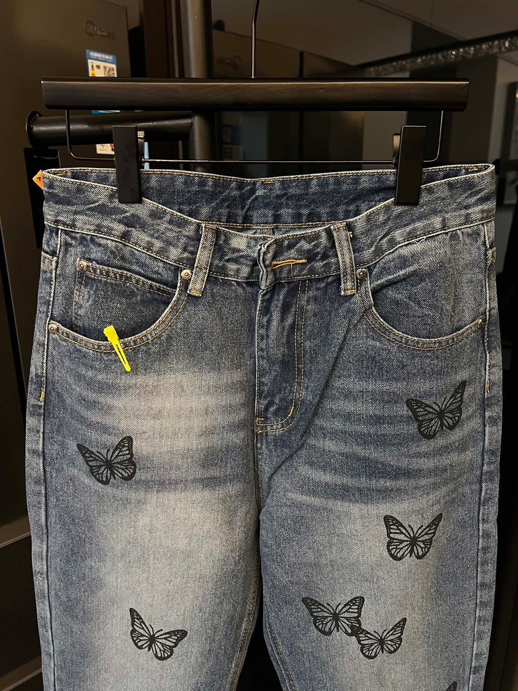 Light blue denim jeans with black butterfly embroidery, stitched pockets, and button closure