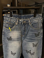 Light blue denim jeans with black butterfly embroidery, stitched pockets, and button closure