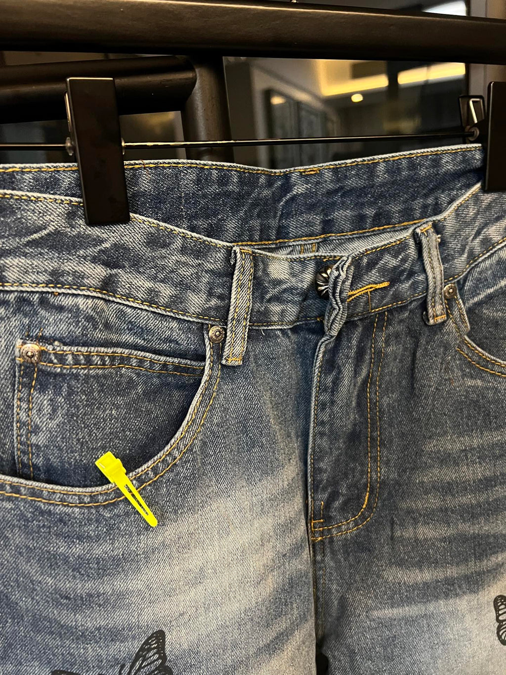 Light blue denim jeans with front fly, belt loops, and black butterfly embroidery detail
