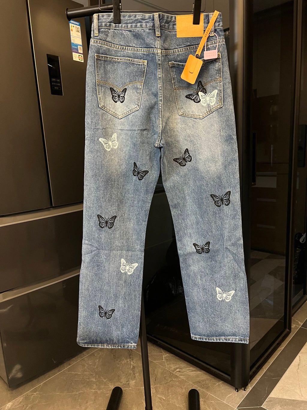 Light wash denim jeans with butterfly patches on the legs, front view on hanger