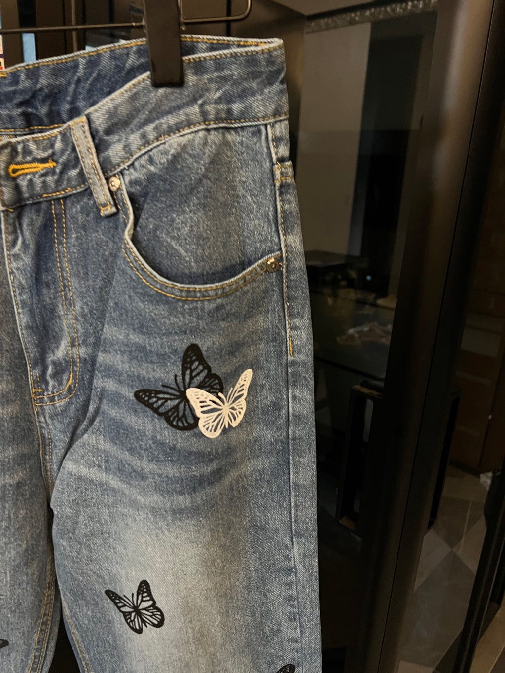 Light wash denim jeans with a butterfly patch on the thigh, side pocket detail
