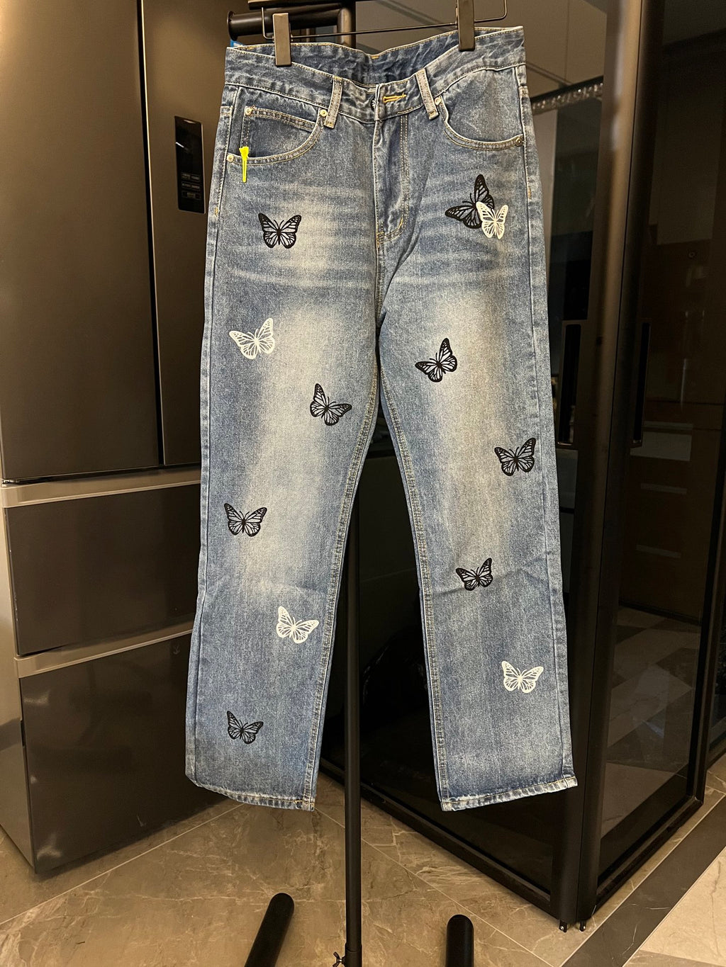 Light wash denim jeans with black and white butterfly patches, straight front view