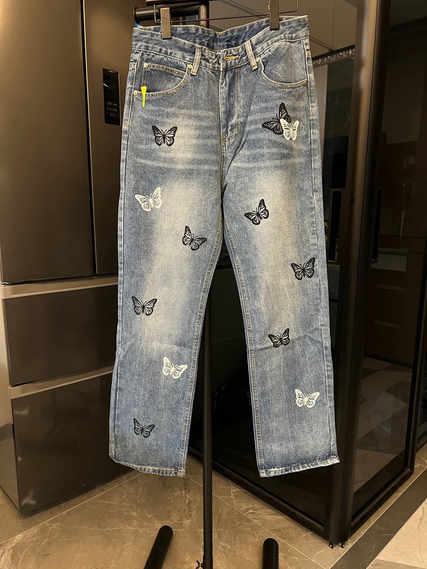 Light wash denim jeans with black and white butterfly patches, straight front view