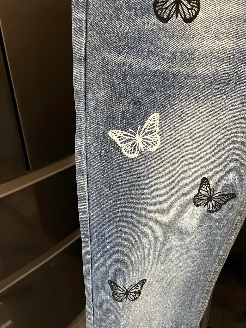 Light wash denim jeans with butterfly patches, close-up of one leg