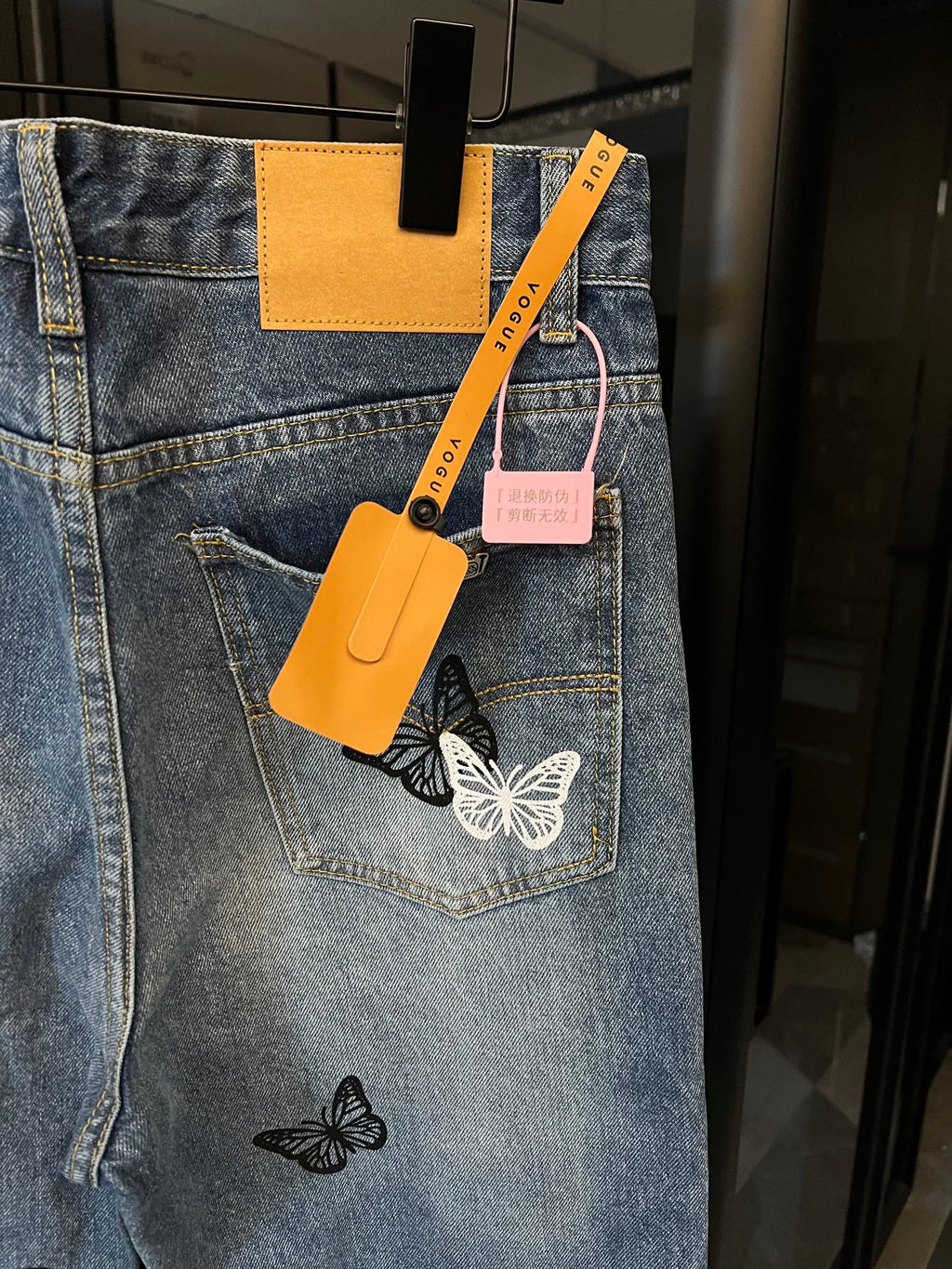 Light wash denim jeans with butterfly patches, back pocket and hanging tags visible