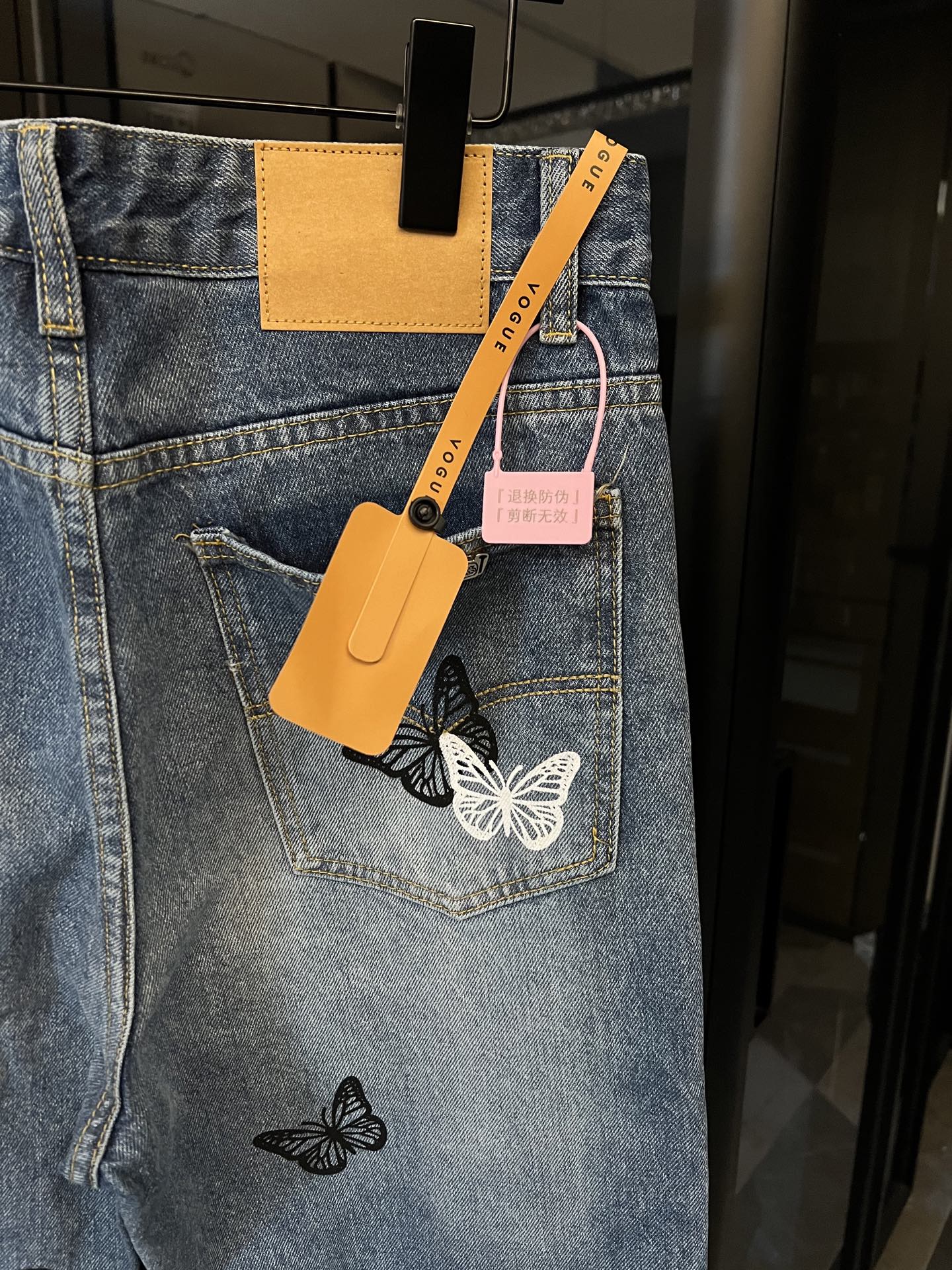 Light wash denim jeans with butterfly patches, back pocket and hanging tags visible
