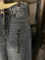 Denim jeans close-up, light blue wash, curved pocket seams, vertical logo embroidery