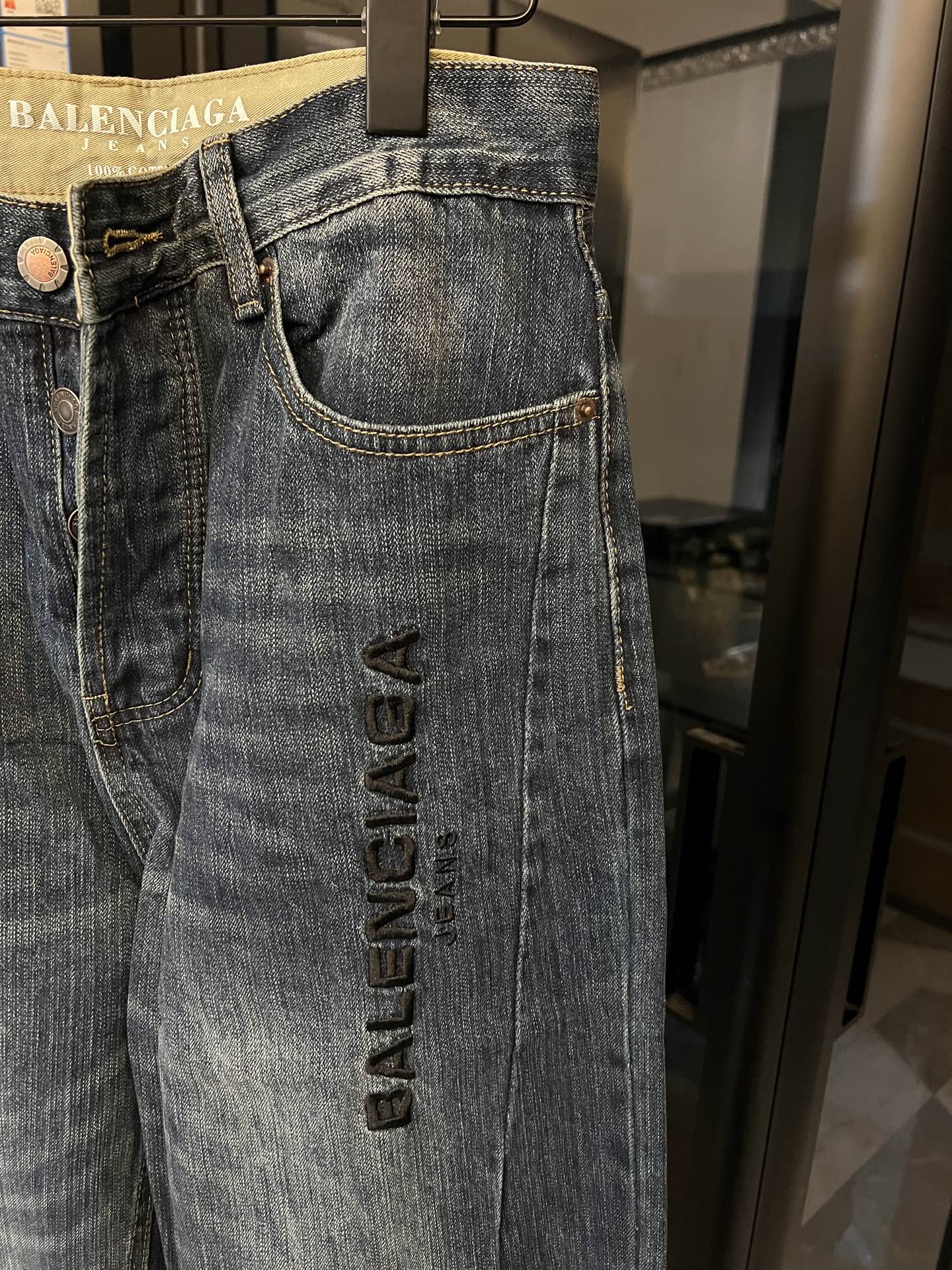 Denim jeans close-up, light blue wash, curved pocket seams, vertical logo embroidery