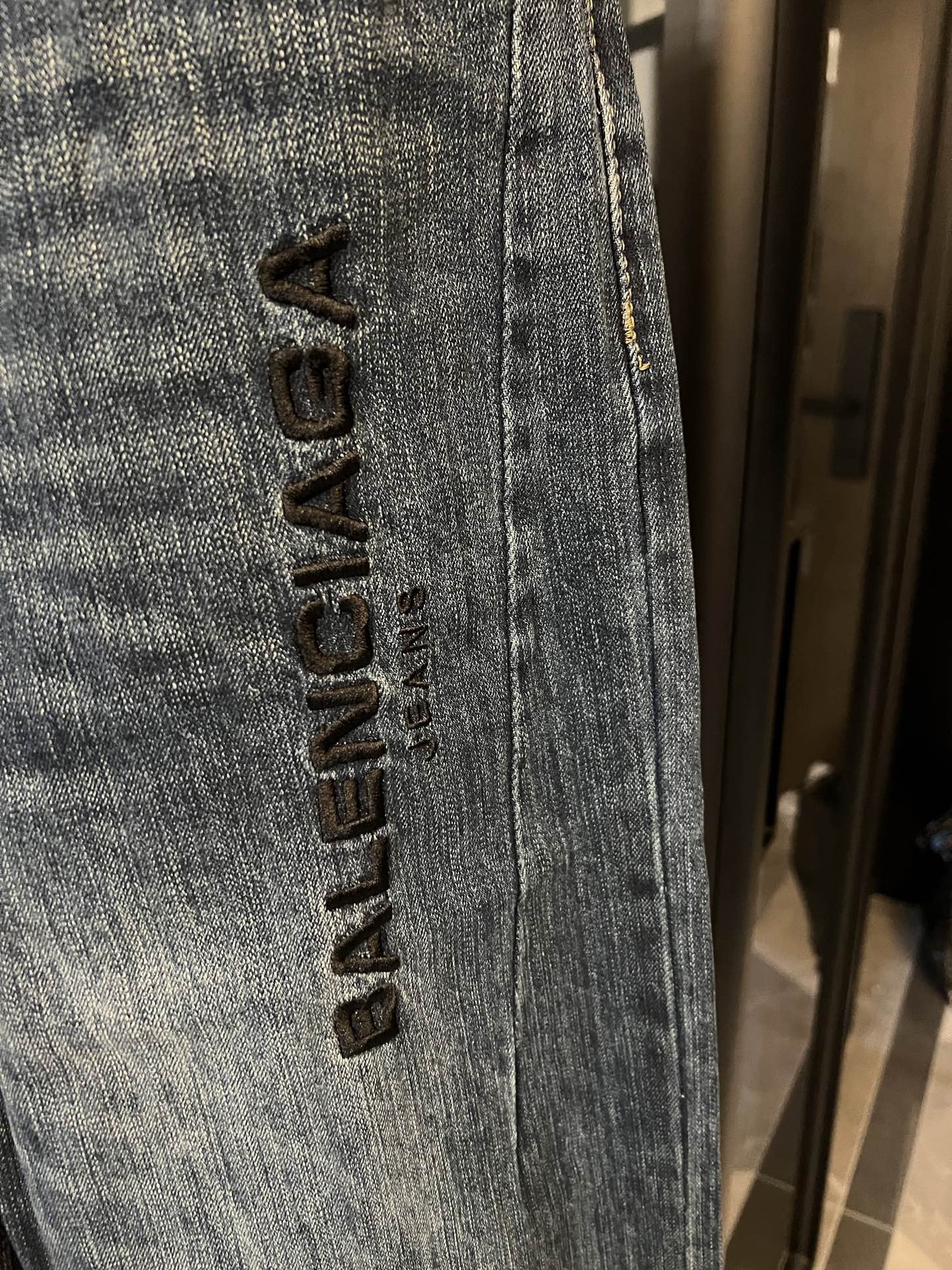 Denim jeans close-up, vertical black logo embroidery on light blue leg seam