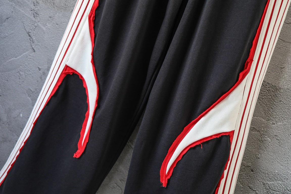 Black track pants with curved red-accent cutout on side panel and white stripes