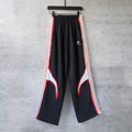 Black track pants with red and white side stripes, wide leg and elastic waistband
