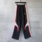Black track pants with red and white side stripes, wide leg and elastic waistband
