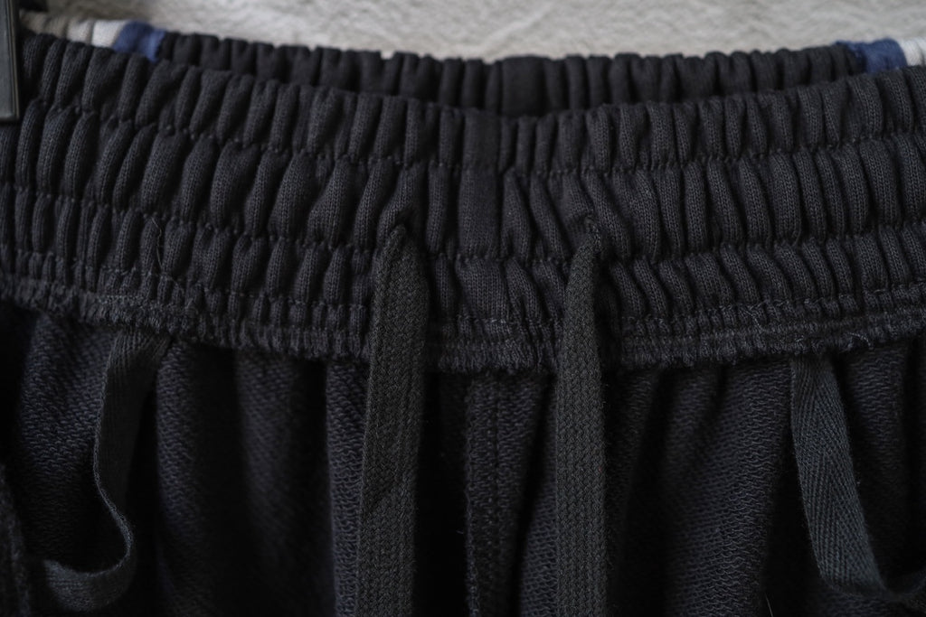 Black track pants waistband with elastic, textured fabric and stitched pleats