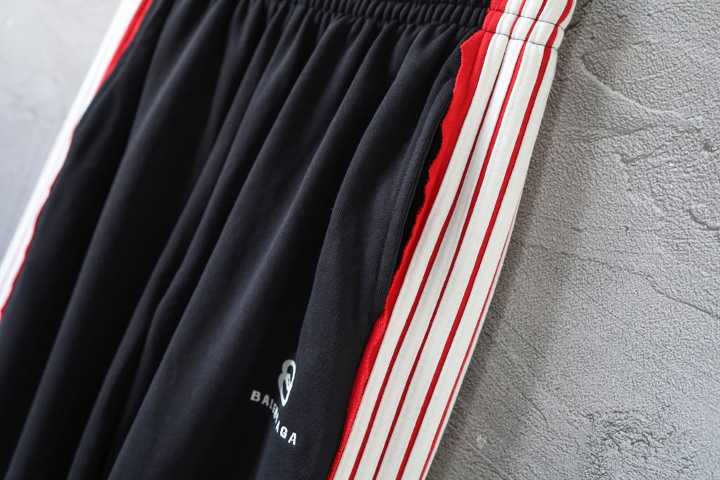 Black track pants with red and white side stripes and gathered front pleats