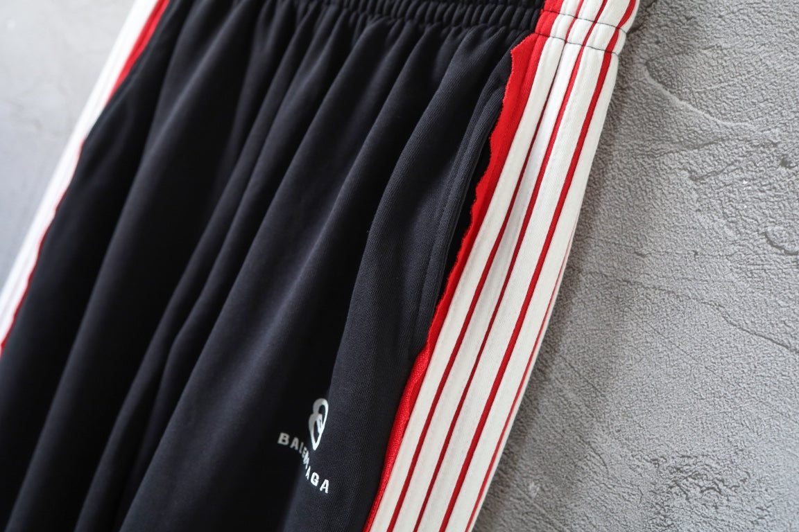 Black track pants with red and white side stripes and gathered front pleats