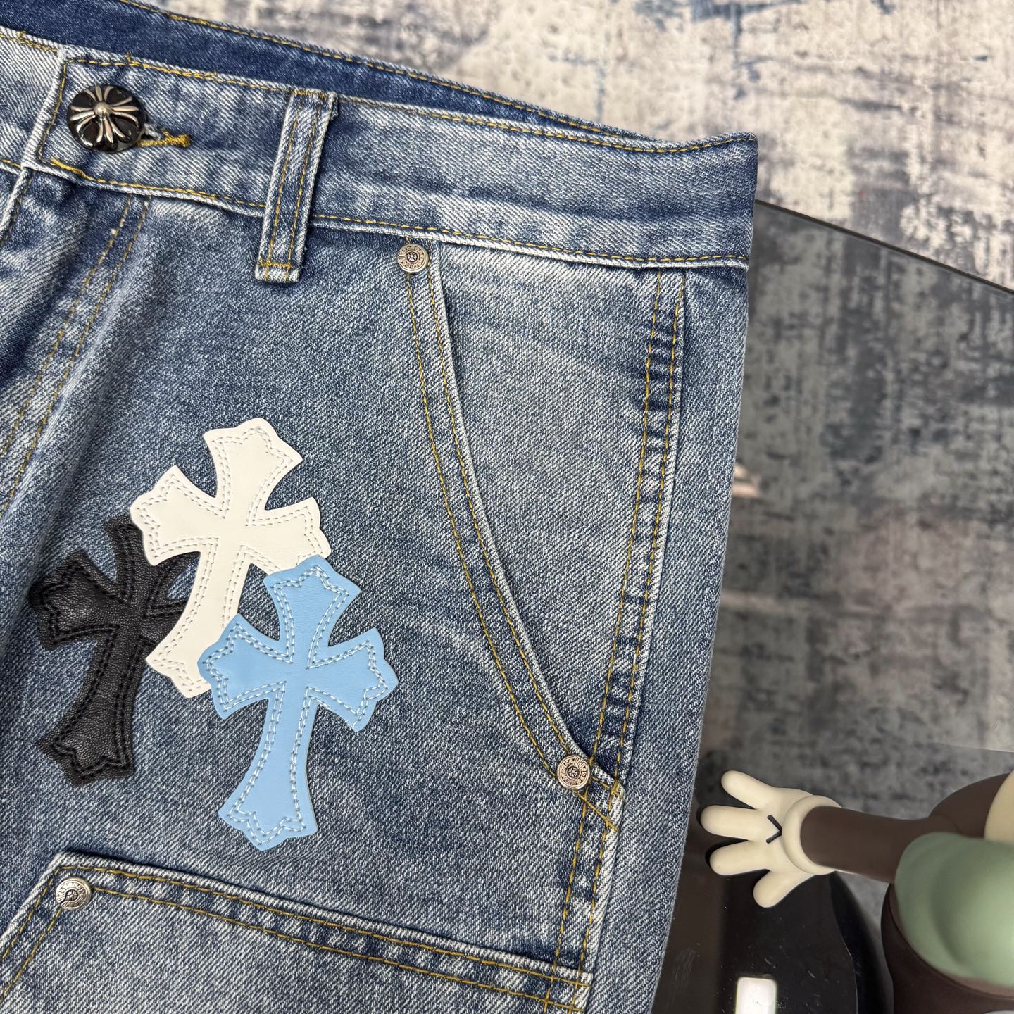 Light blue denim pants with cross applique patches on front and side pockets