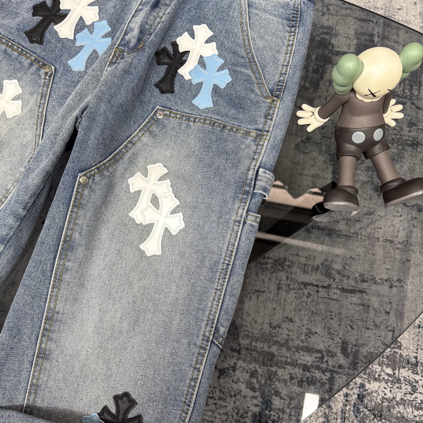 Light blue denim pants with cross applique patches across the legs