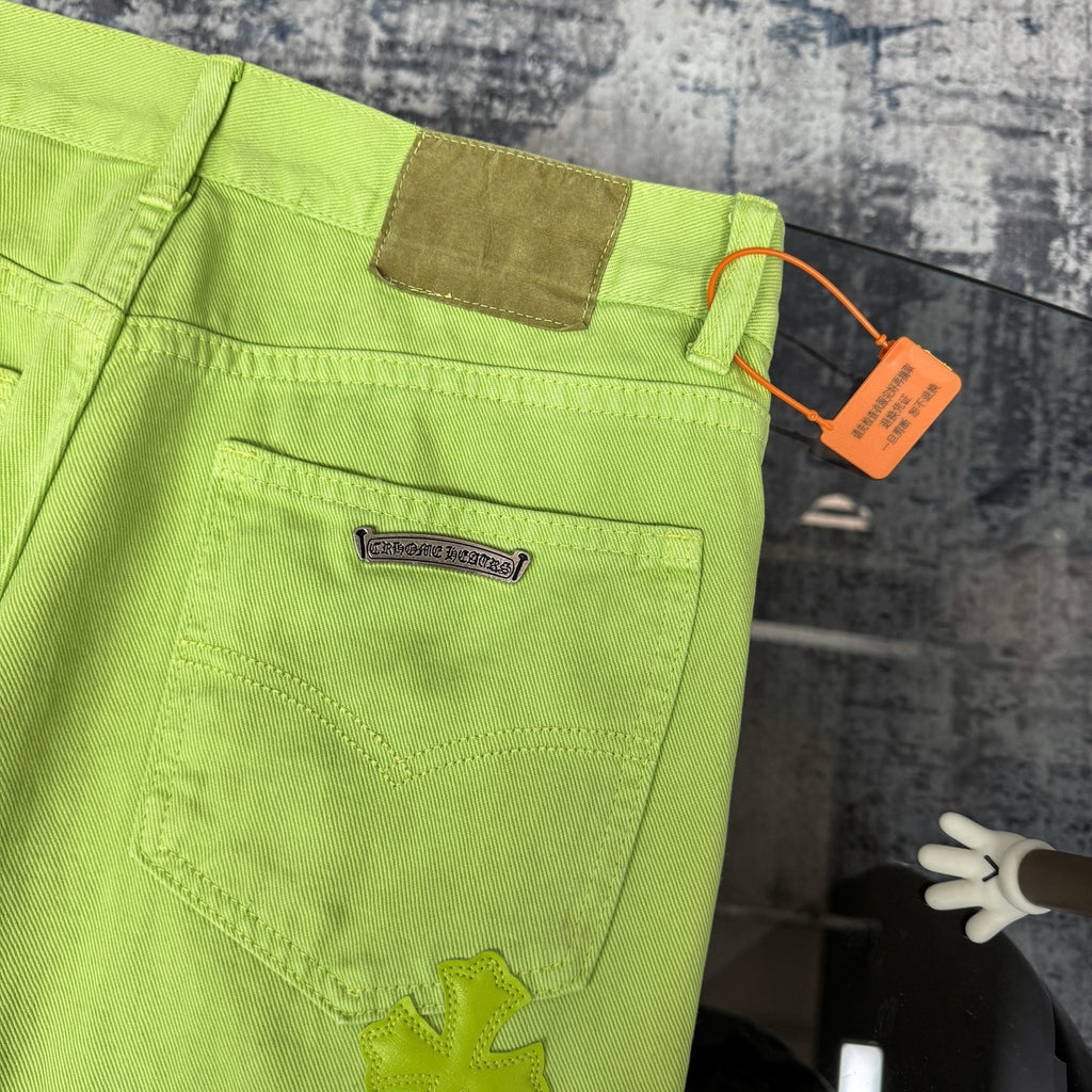 Lime green pants with patch-style pocket and stitched seams, plus small black cross detail