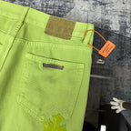 Lime green pants with patch-style pocket and stitched seams, plus small black cross detail