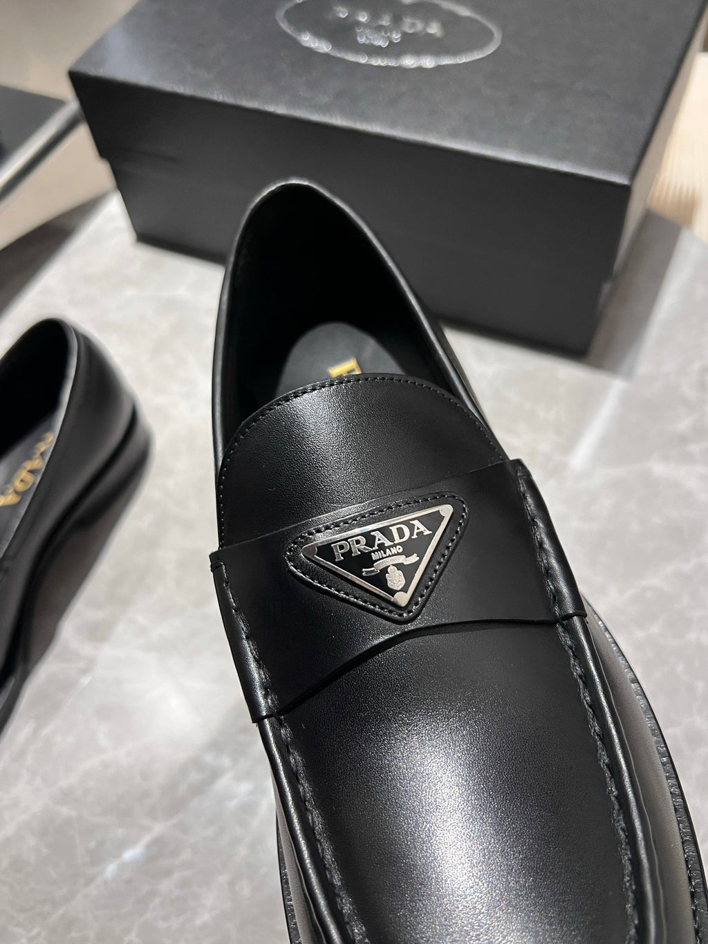 Black leather loafer upper close-up with Prada logo patch and stitching