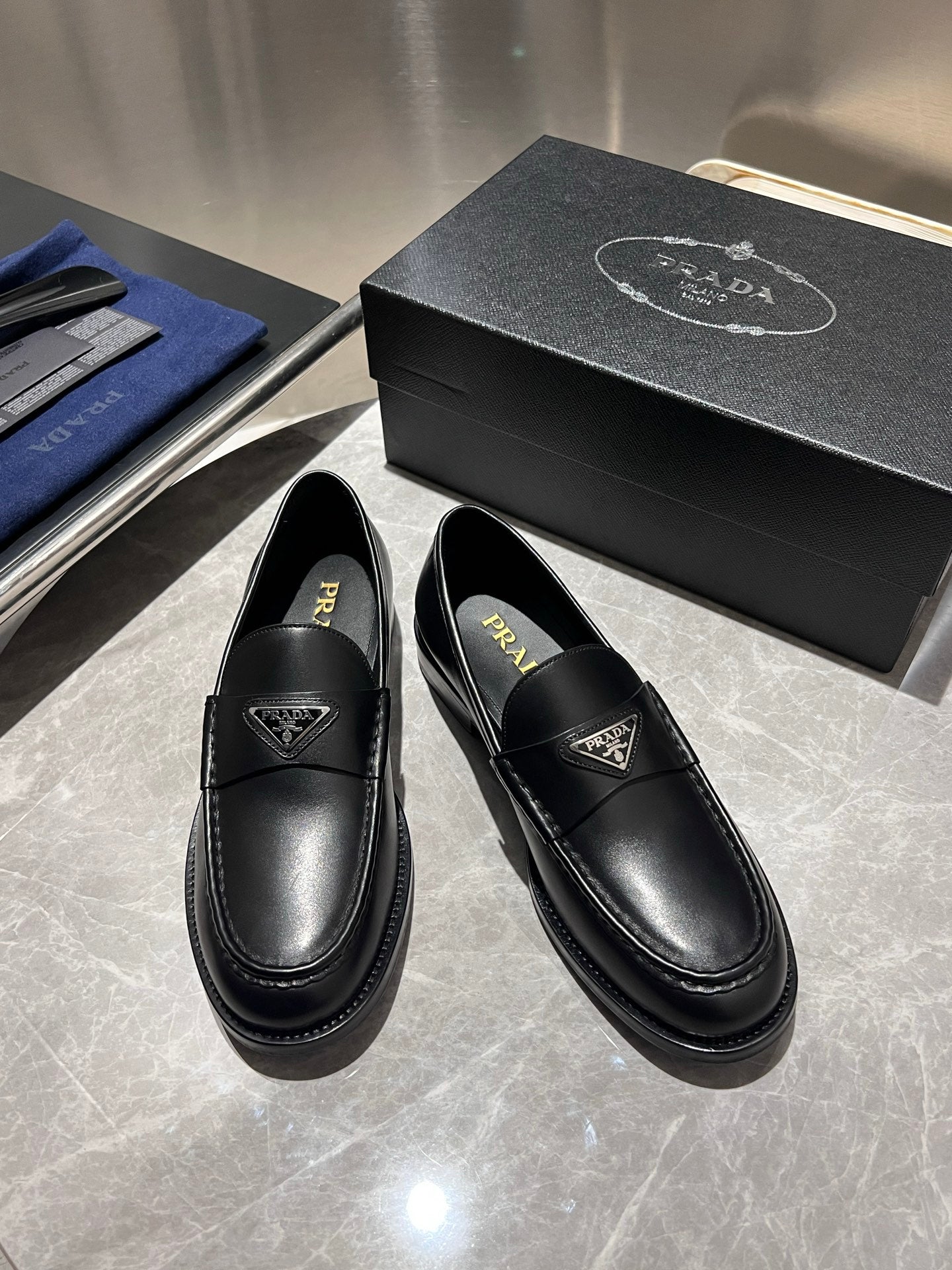 Black leather loafers, front view with decorative strap and Prada logo