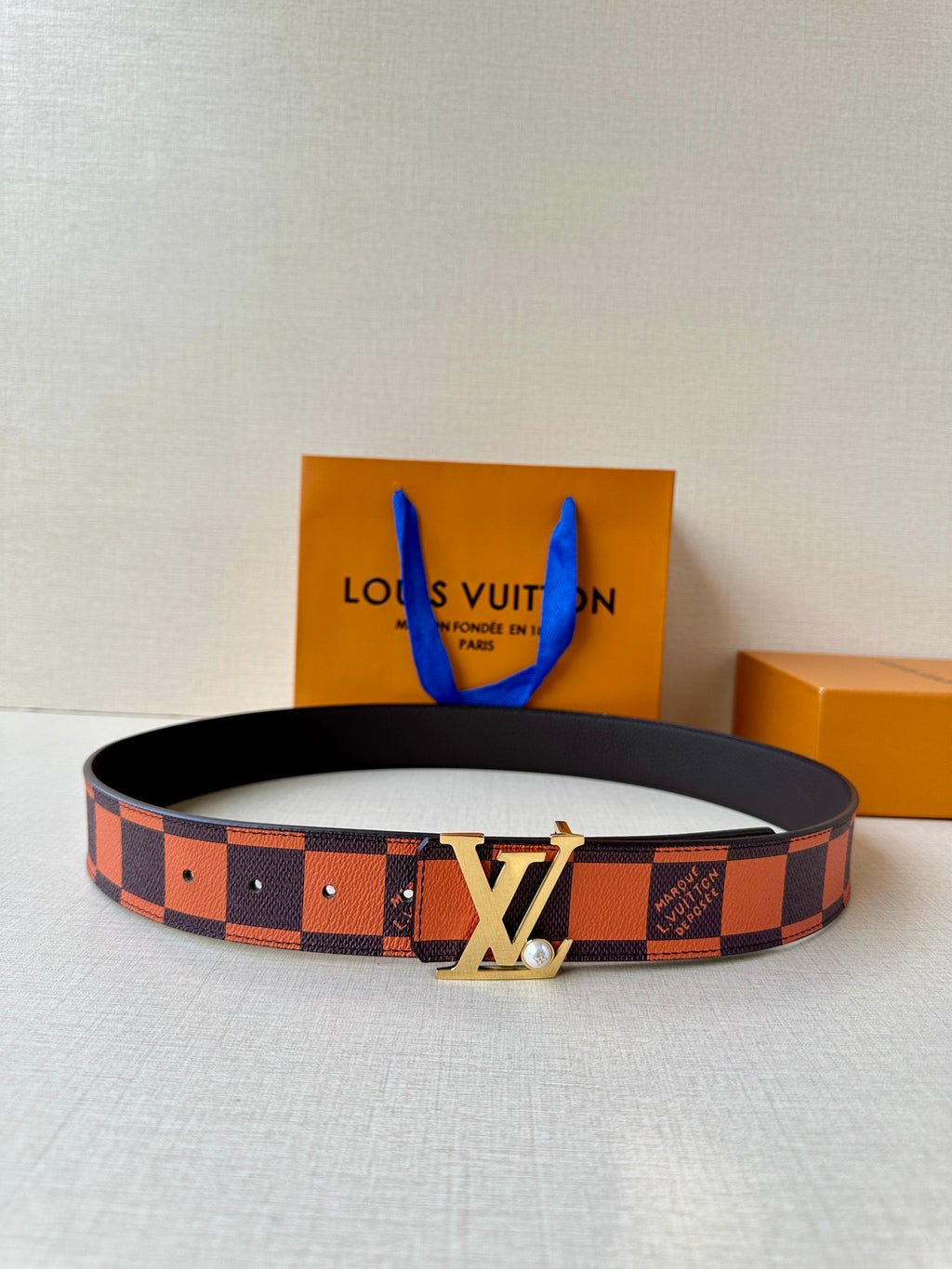 Louis Vuitton belt with orange and brown check strap and gold-tone LV buckle.