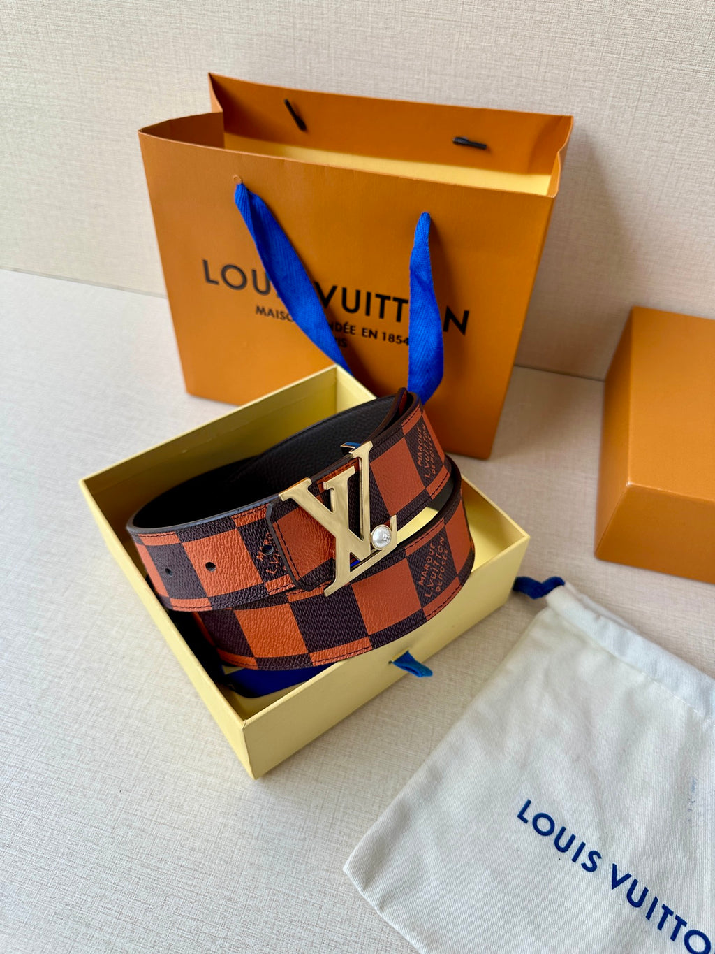 Louis Vuitton belt with patterned strap and large gold-tone LV buckle on a pouch.
