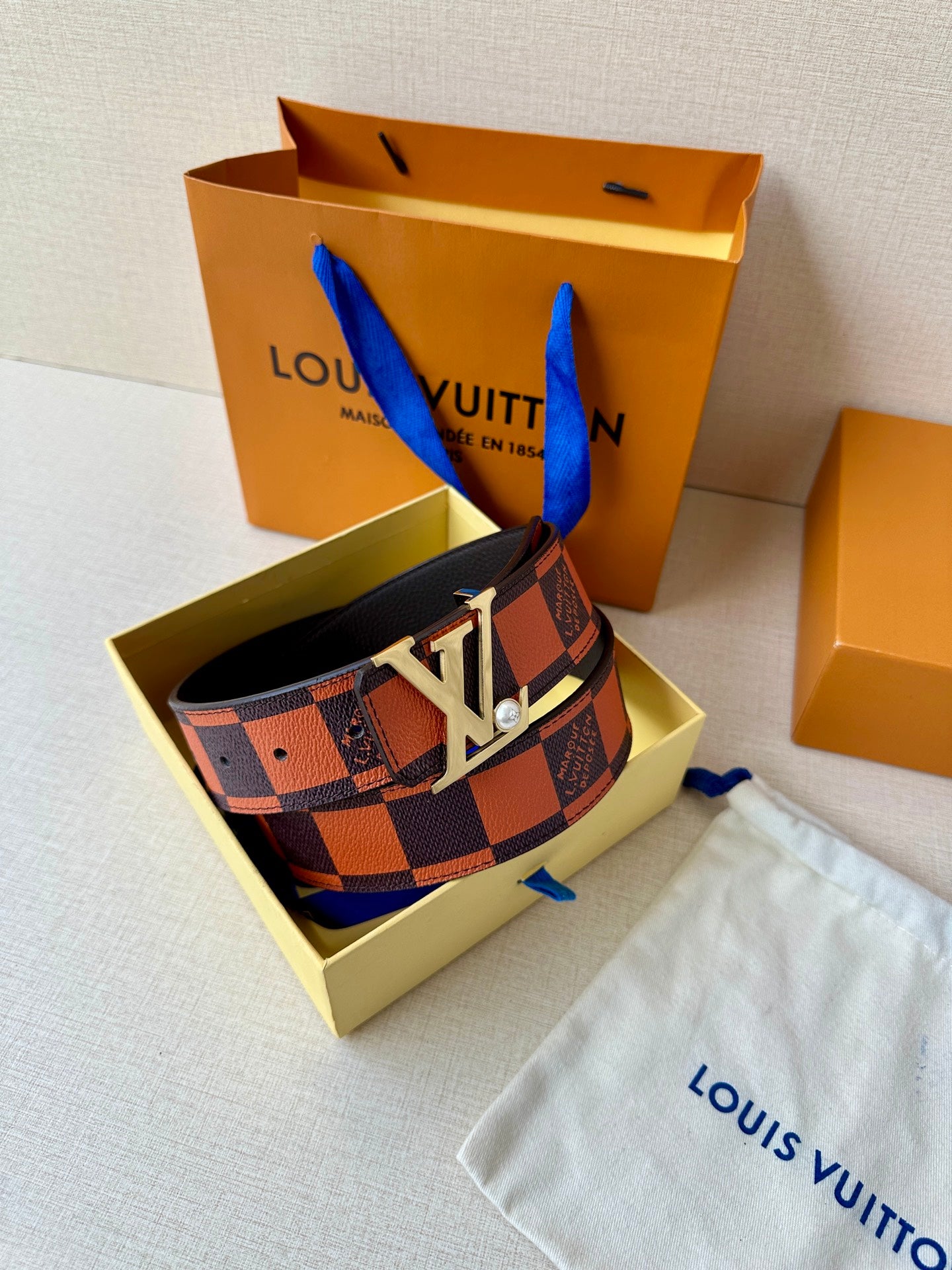 Louis Vuitton belt with patterned strap and large gold-tone LV buckle on a pouch.