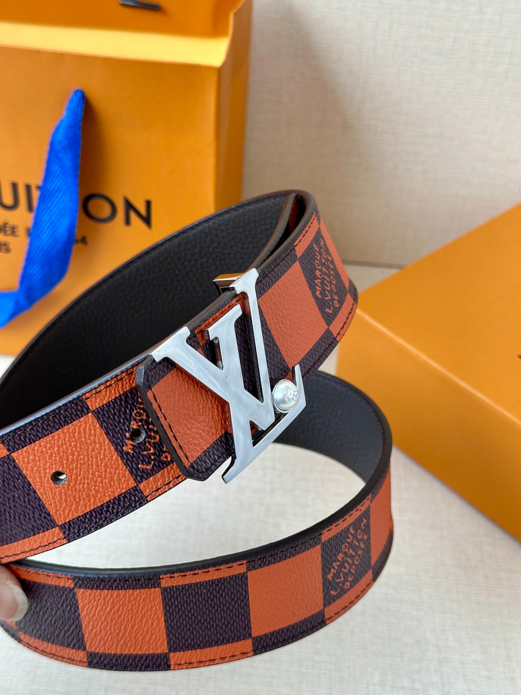 Louis Vuitton belt close-up: orange-brown check strap with silver-tone LV buckle.