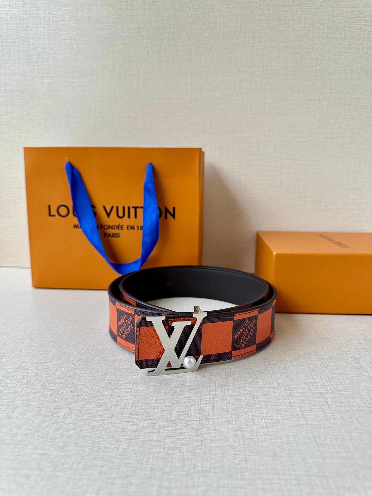 Louis Vuitton belt with orange-brown check strap and gold LV buckle on a table.