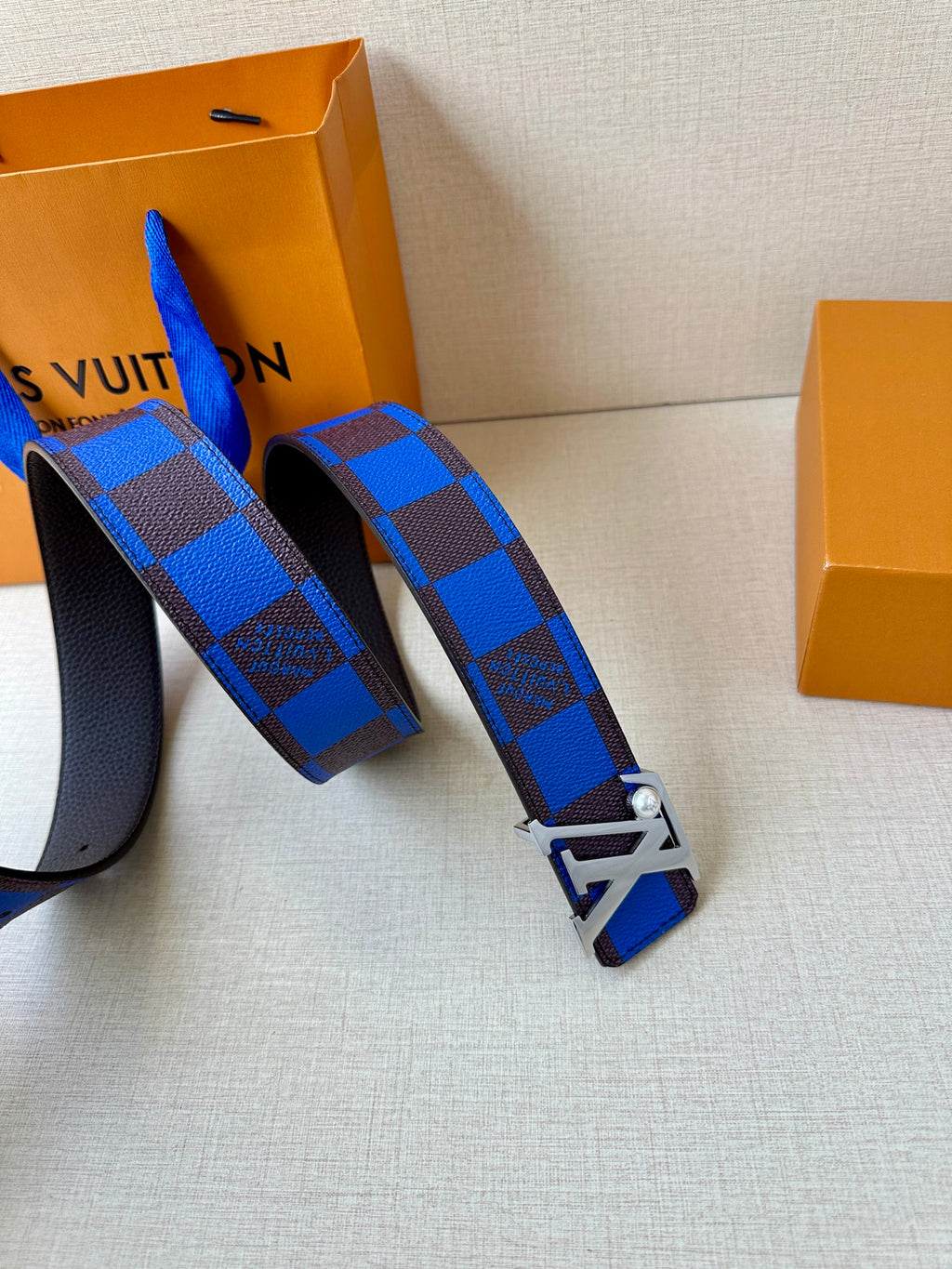 Louis Vuitton belt laid out with blue check strap and LV logo metal buckle.