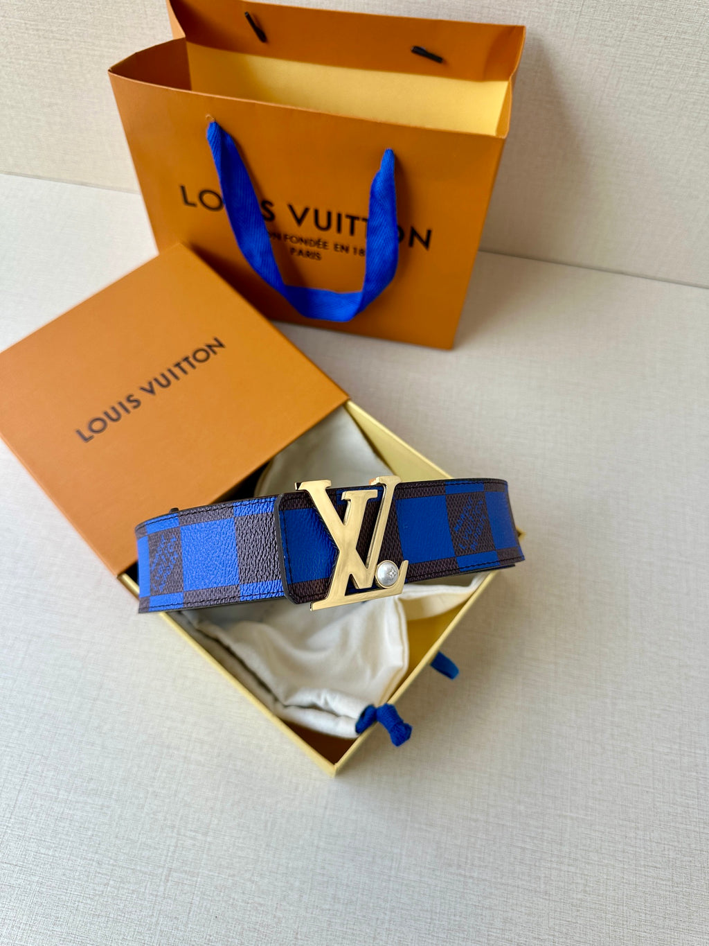Louis Vuitton belt with blue check strap and gold-tone LV buckle on pouch.