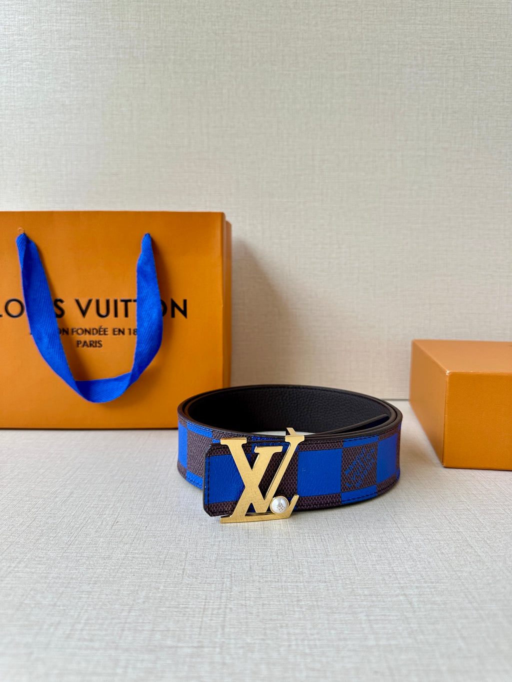 Louis Vuitton belt with blue check strap and large gold-tone LV buckle.