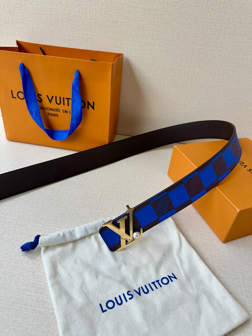 Louis Vuitton belt extended with blue check strap and LV logo buckle detail.