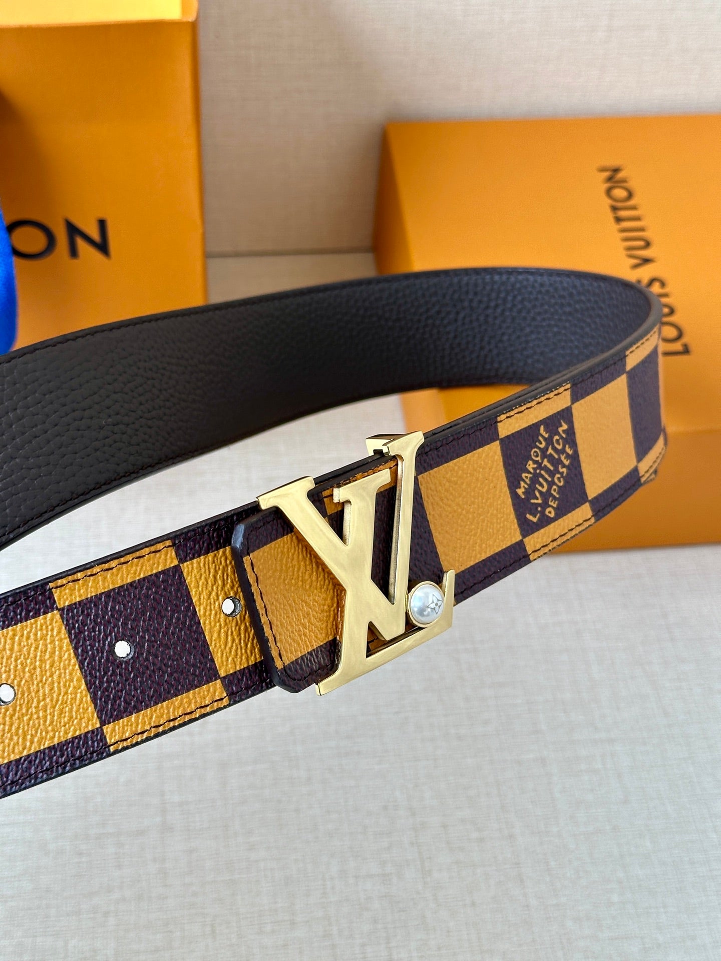 Check-pattern belt showing gold-tone LV buckle and perforated strap holes