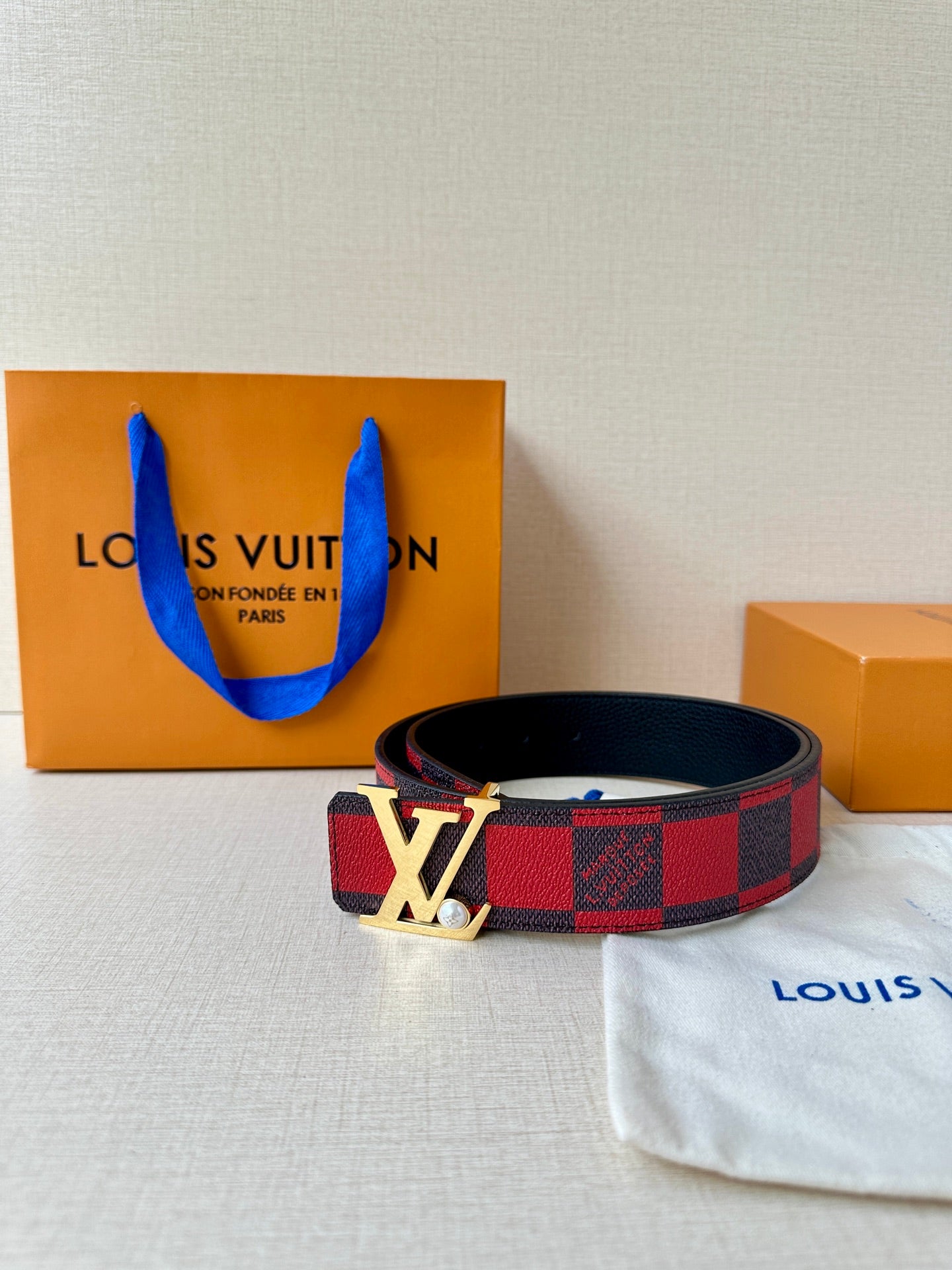 Louis Vuitton belt with red-and-black check pattern and silver LV buckle on dark strap