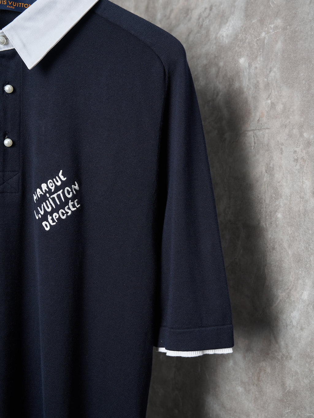 Navy polo with embroidered text patch on chest and white sleeve cuff.